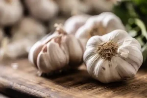 You Uploaded image Copilot The image shows several garlic bulbs on a rustic wooden surface. Each bulb is whole, with its papery outer skin intact. The image has a shallow depth of field, focusing on the bulbs in the foreground while the background is slightly blurred. Garlic is such a staple in cooking, not to mention all the health benefits.