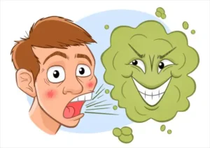 The image shows a cartoon depiction of a person with a blurred face and a green, cloud-like character with a mischievous expression. The green character appears to be representing bad breath, as it is positioned near the person’s mouth and has a sinister smile. The image is likely illustrating the concept of bad breath in a humorous and exaggerated manner. There is no text or math problem present in the image.